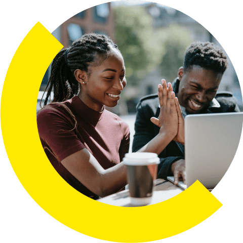 Two people sitting outdoors high fiving in front of a laptop.